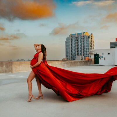 Pregnant woman in red flying maternity dress on building rooftop